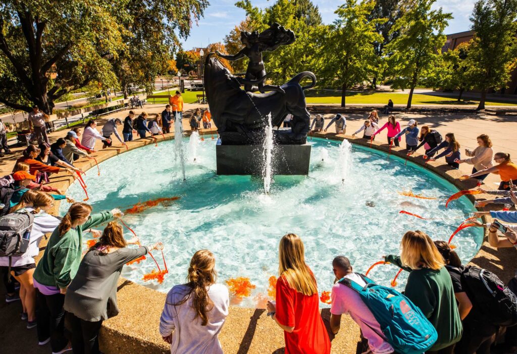 Students gather around the Europa and the Bull fountain to dye the water orange during Homecoming Week