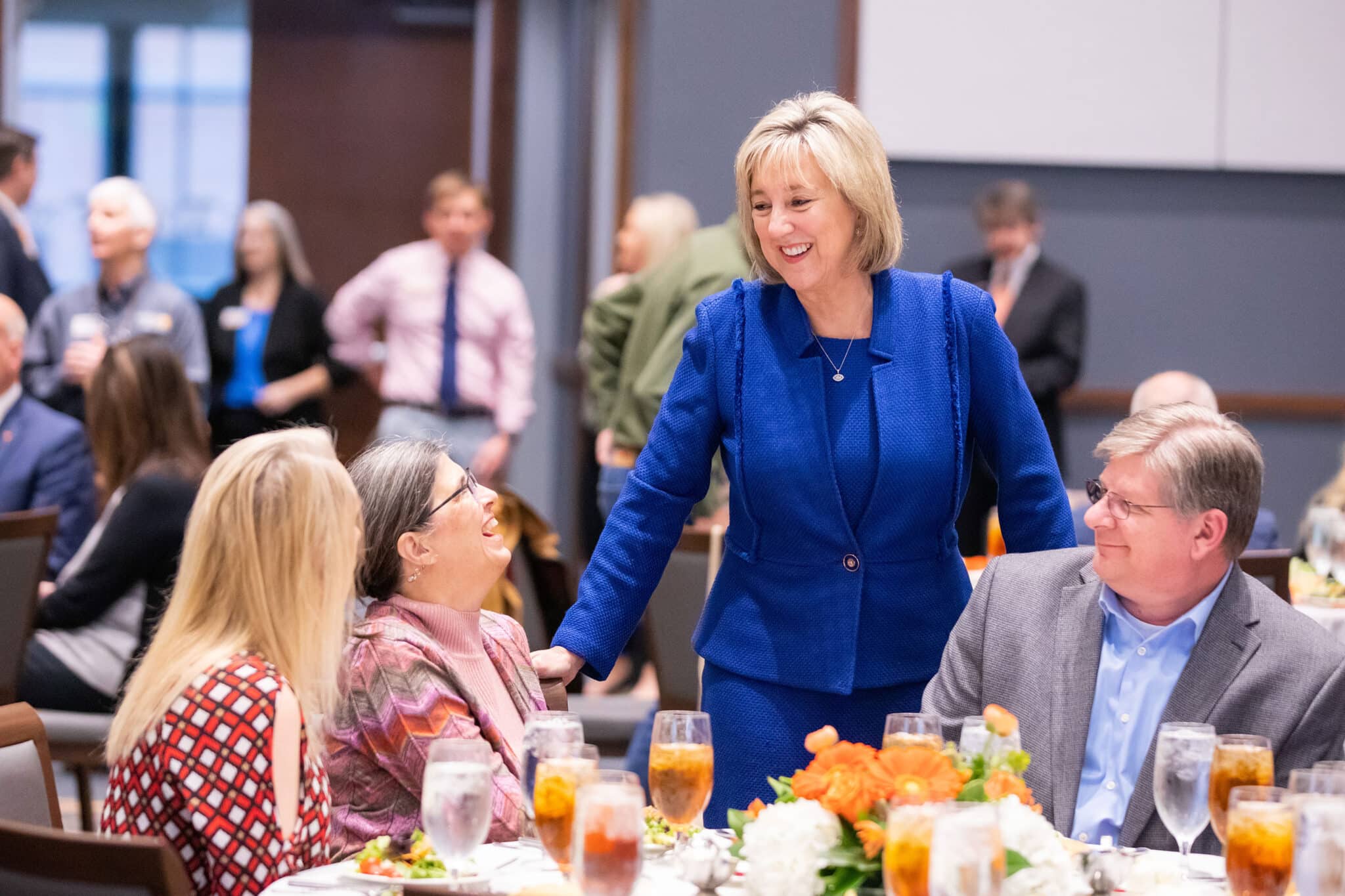 Chancellor Donde Plowman, smiling and wearing a blue suit, visits with employees at a dinner