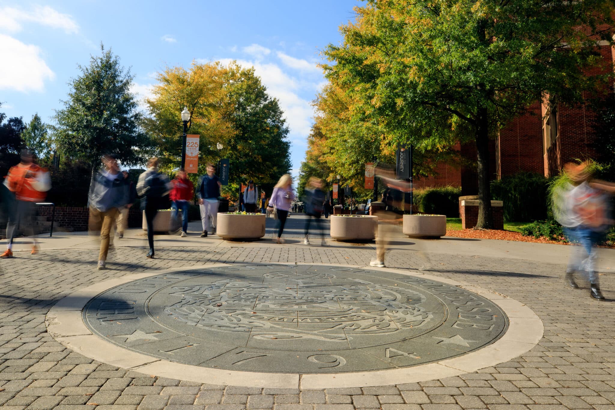 Students walk past the university seal on the Pedestrian Walkway