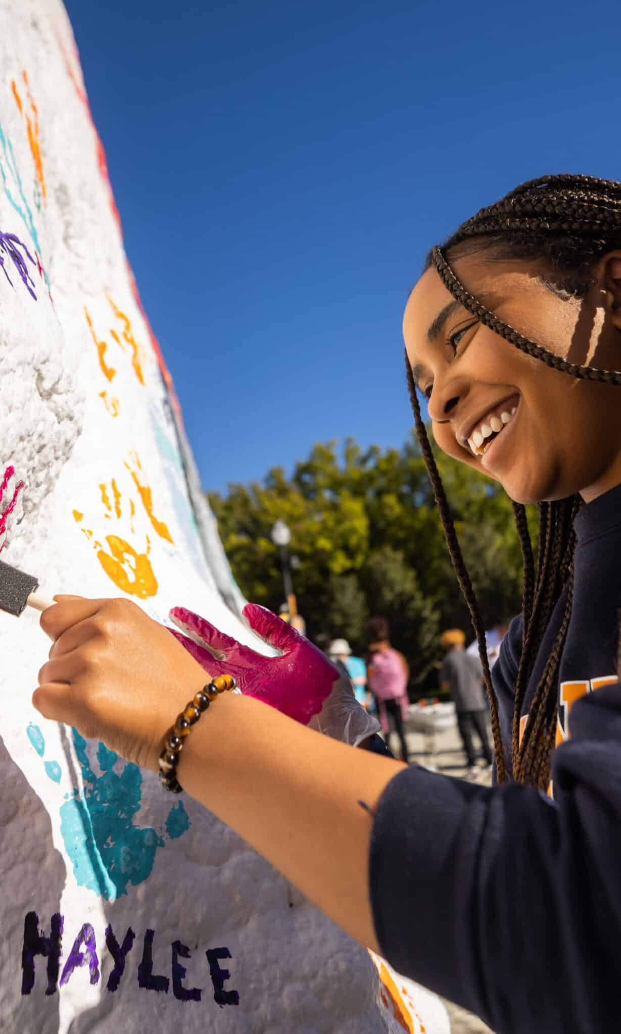 A smiling student applies paint to the Rock