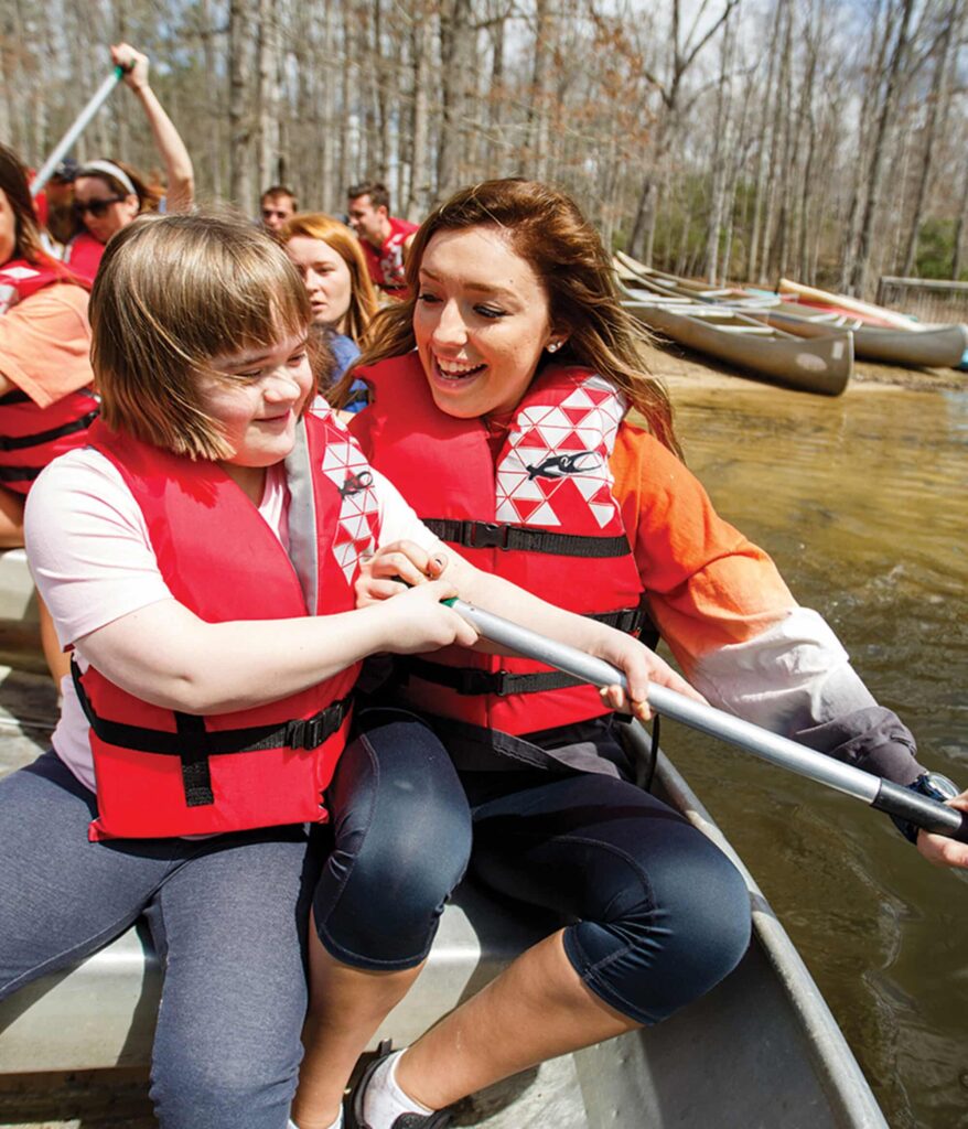 A UT student working with Camp Koinonia helps a child use an oar to propel a canoe