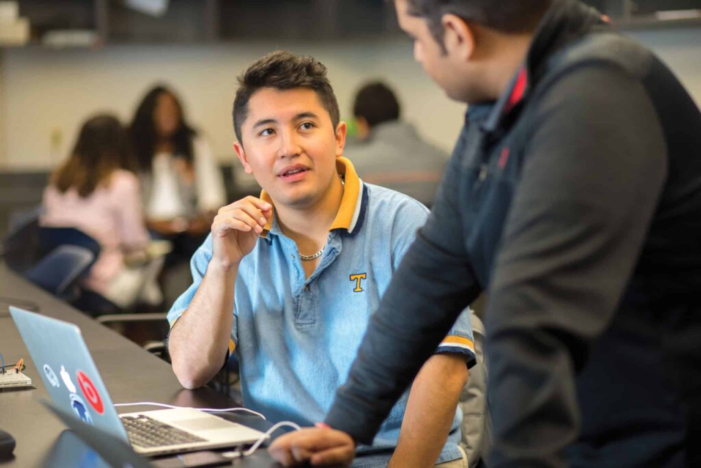 Two graduate students with a laptop engage in a discussion