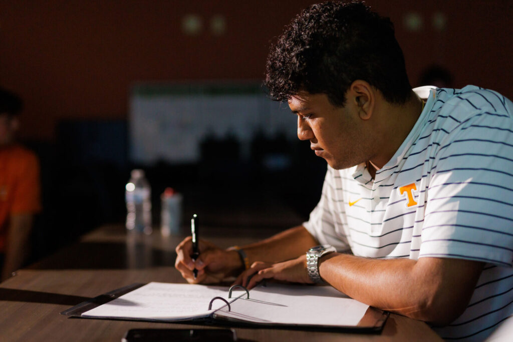 A student sits at a table in the sunlight, working on some papers in a three-ring binder