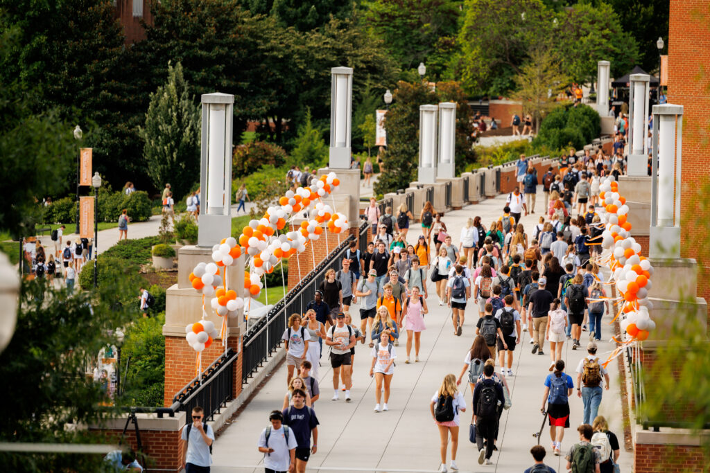 Students walk along a busy Ped walkway bridge decorated with orange and white balloons