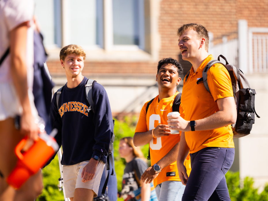 Students wearing UT merchandise walking across campus, laughing and talking