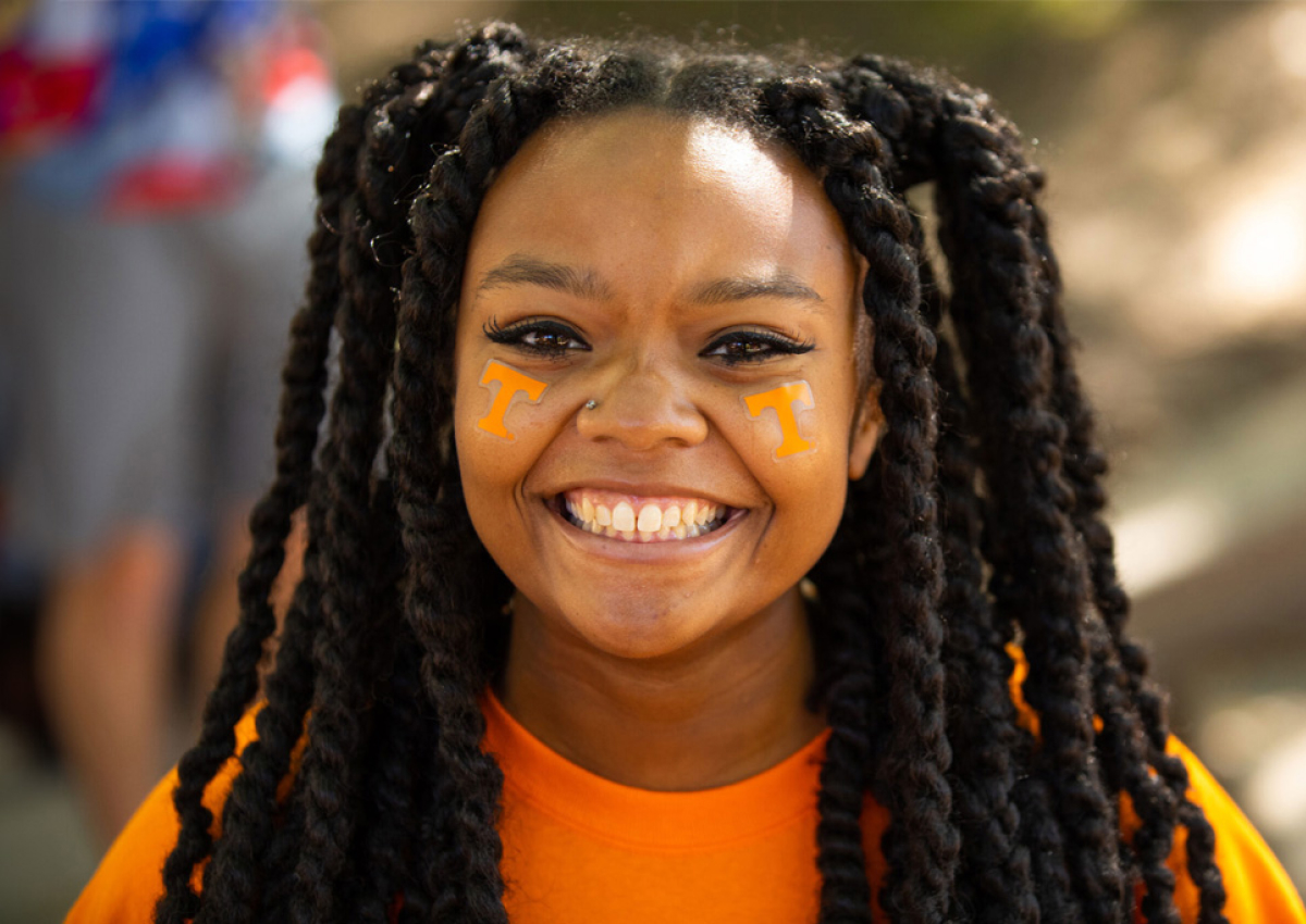A smiling student with orange facepaint and super cute spiral braids wearing an orange t-shirt