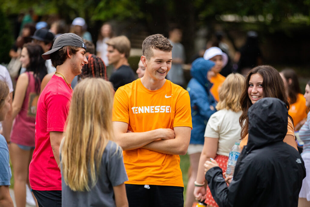 A tall student wearing an orange Tennessee shirt talks to a group of his peers