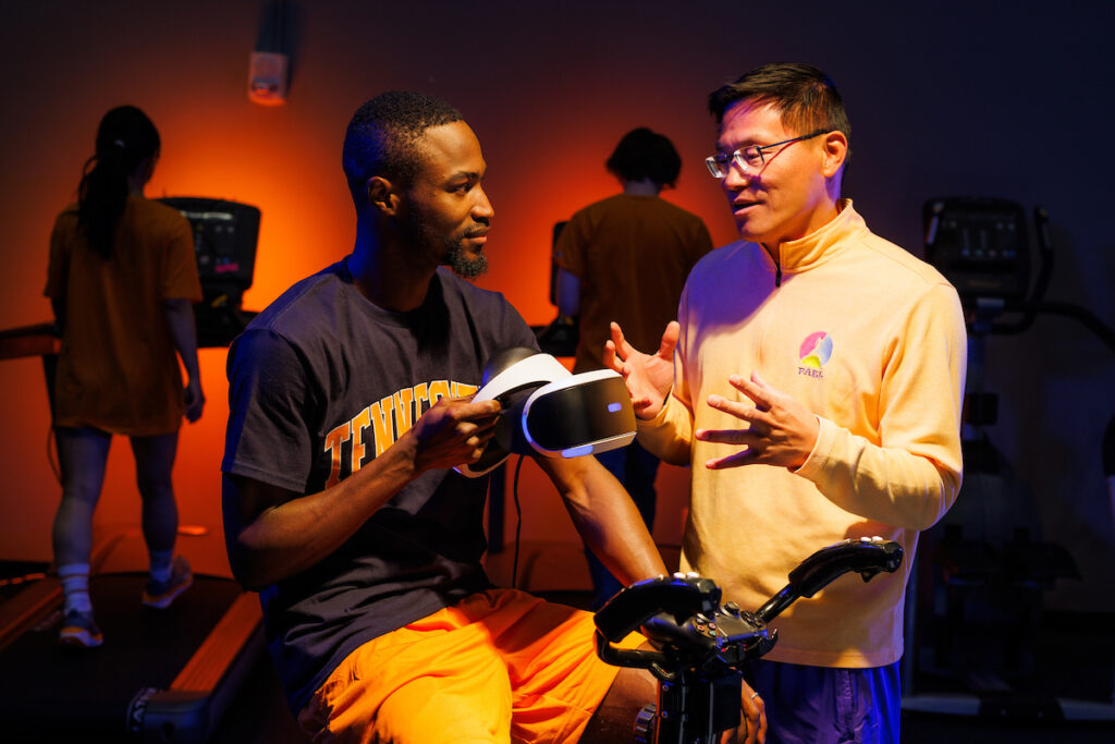 Professor and Department Head Zan Gao talks with kinesiology PhD student John Oginni simulating an experiment using a virtual reality bicycle exercise program in the Physical Activity Epidemiology Lab on January 09, 2025. Photo by Steven Bridges/University of Tennessee.