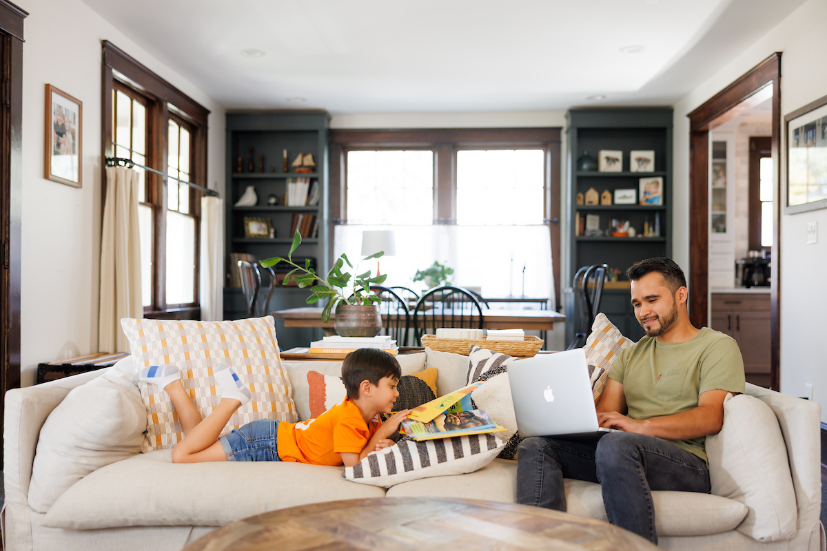 A father sits on a couch and works on a laptop as his son sits next to him reading a book during a Digital Learning produced lifestyle video/photoshoot inside a home in Fountain City by the Office of Communications and Marketing Department at the University of Tennessee on October 02, 2024. Photo by Steven Bridges/University of Tennessee.