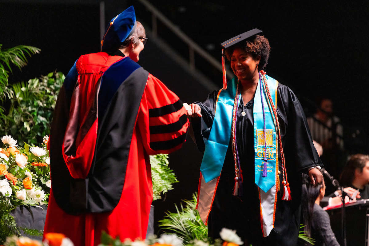 The Dean of the College of Education, Health and Human Sciences, fist bumps a graduate as they walk across the stage