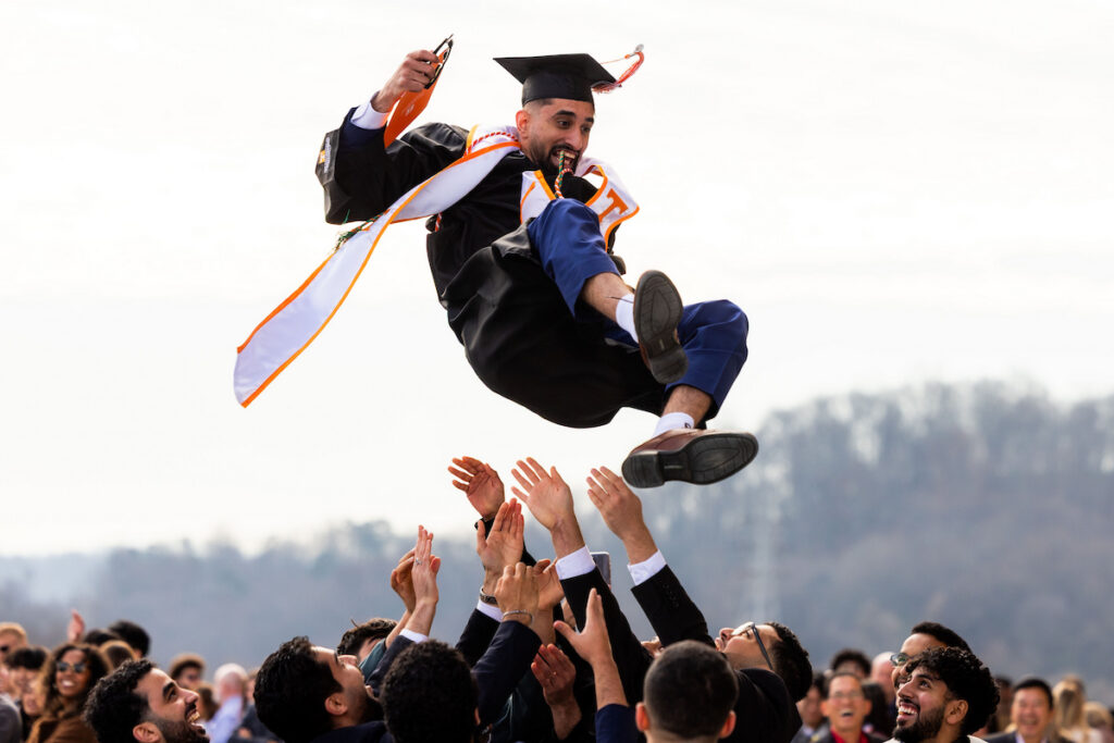A graduate is tossed in the air by friends and family after a commencement celebration.